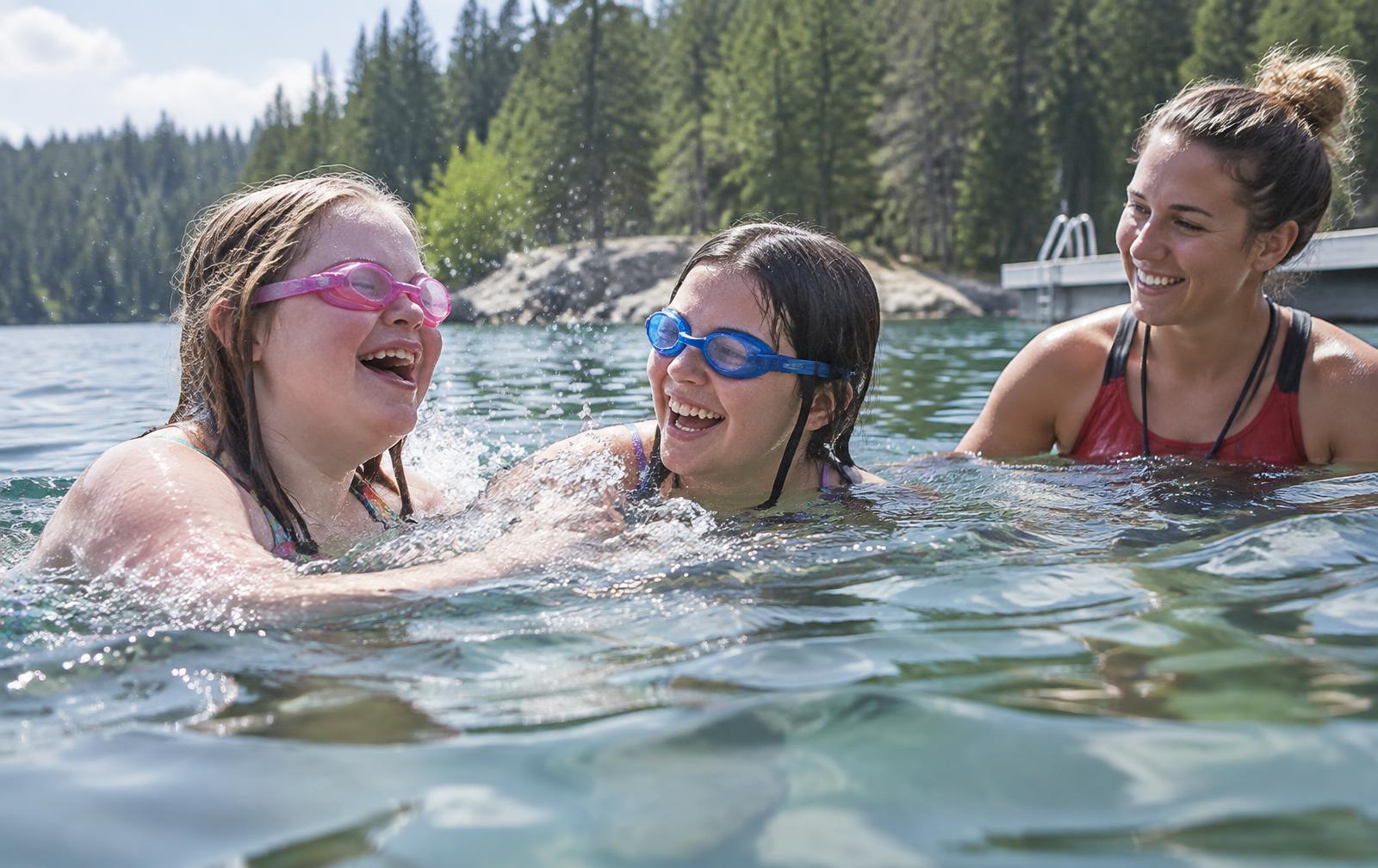 Two teenage girls laughing while swimming in a lake, an instructor in the water beside them